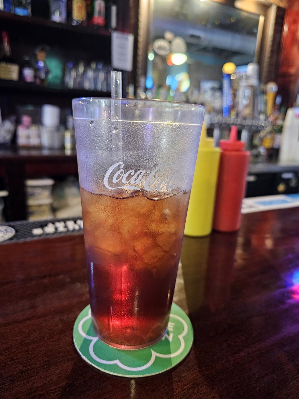 A tall glass of iced drink on the bar, with the back bar and beer taps softly out of focus behind it.